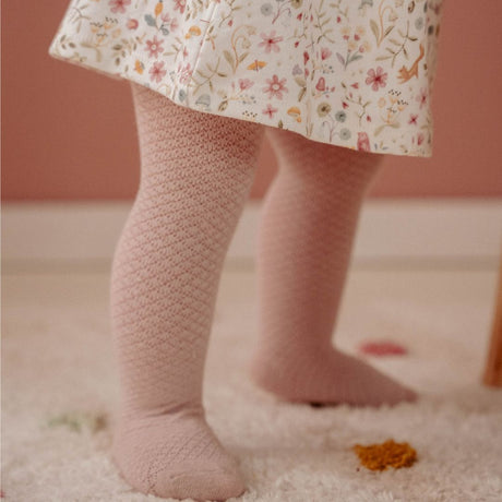 Babyben det med rosa strømpebukser, set på blødt lyst gulvtæppe.