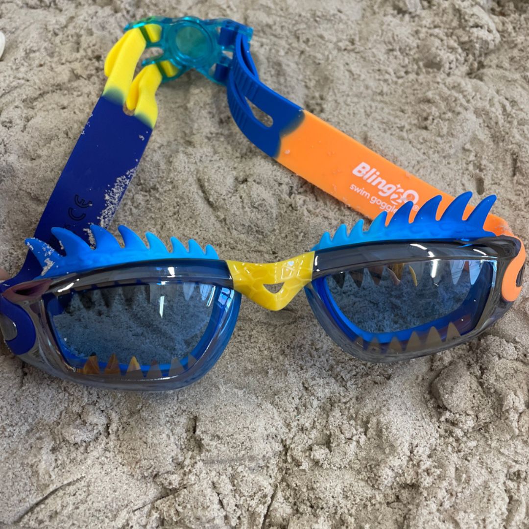 blå svømmebriller dekoreret med drage-takker fra Bling20, set i sand.