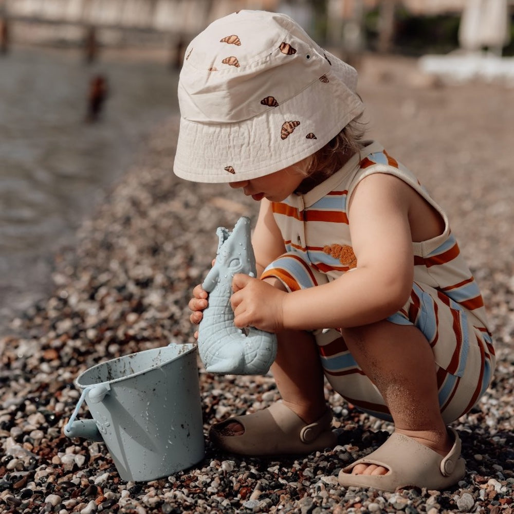 barn på strand med blå vandkande formet som krokodille, og blå spand, perfekt til små hænder